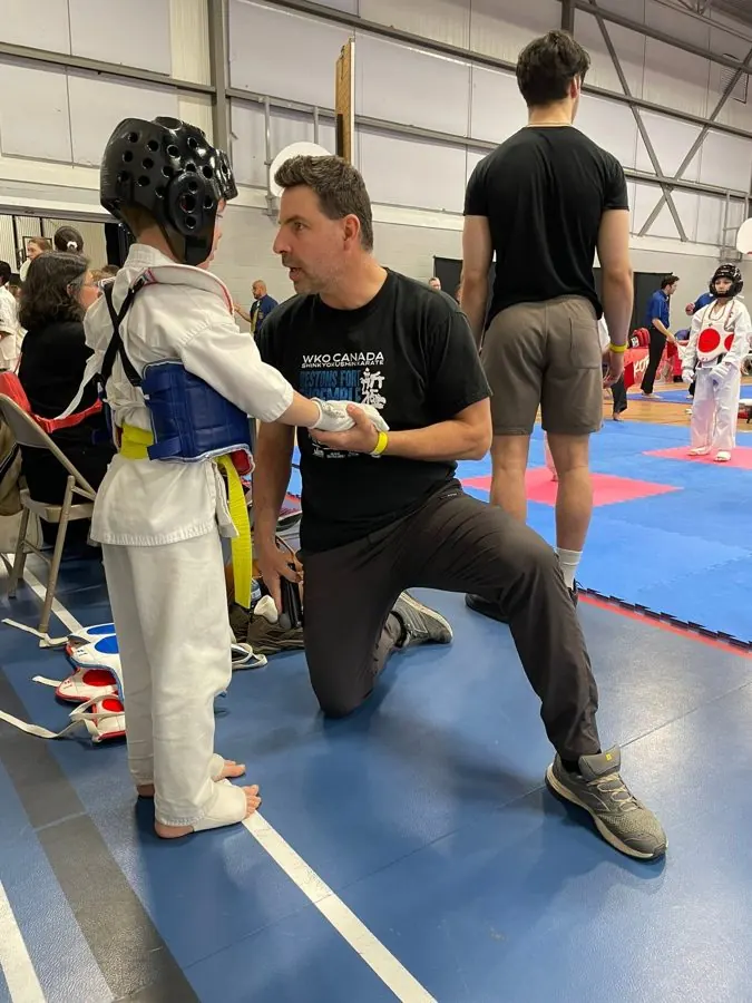 A child in protective gear, coached at the edge of the mat